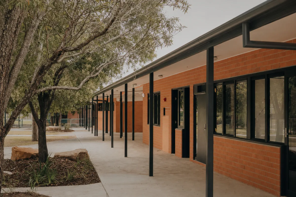 Completed low-rise school classroom block with warm brick walls and covered walkway.