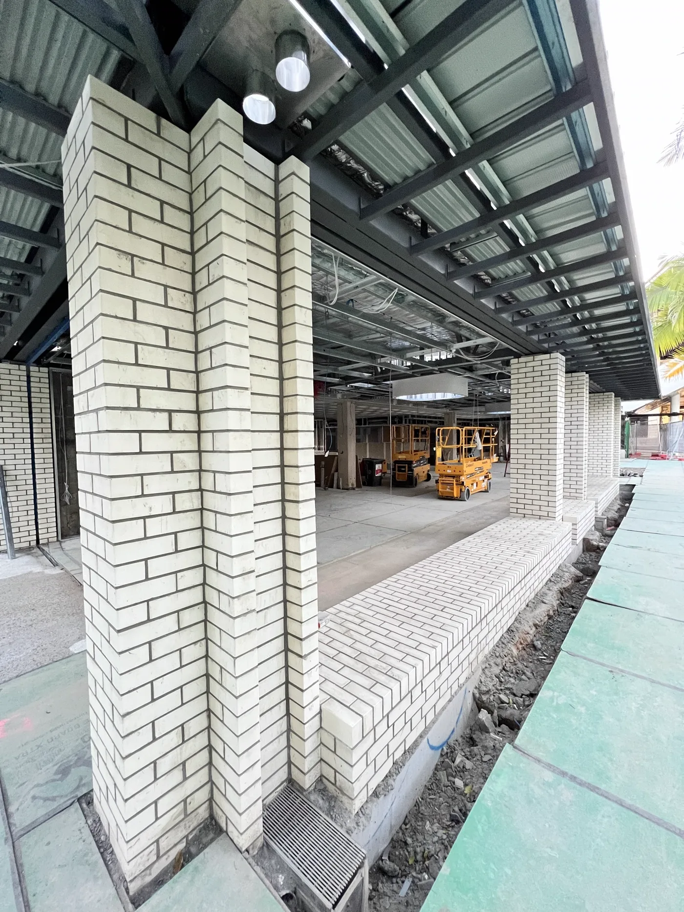 Tall white face-brick columns supporting a steel-framed colonnade, with a herringbone plinth wall alongside.