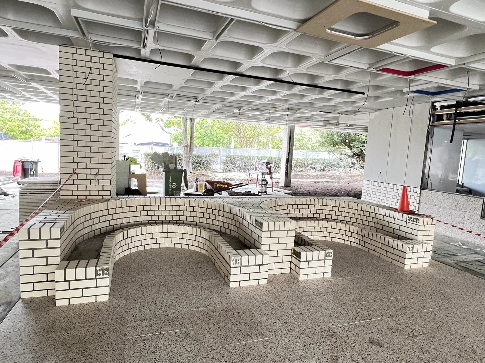Curved white brick seating walls forming an indoor amphitheatre beneath a waffle-slab ceiling.