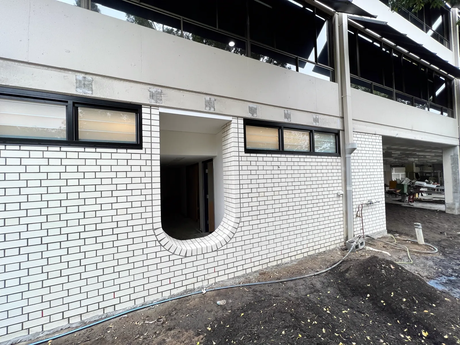 Two-storey white face-brick facade with black window frames and a curved brick entry opening.