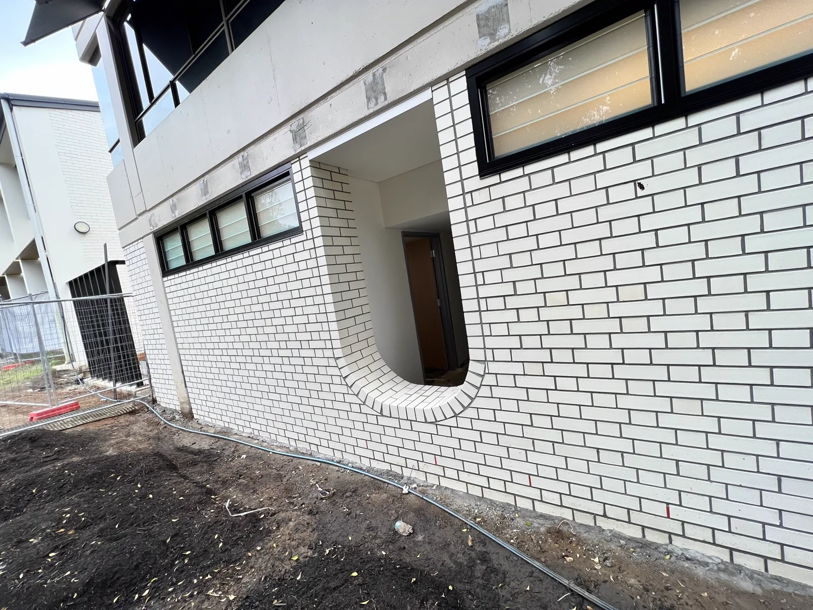 White brick facade with a curved recessed entry, black-framed windows and concrete banding above.