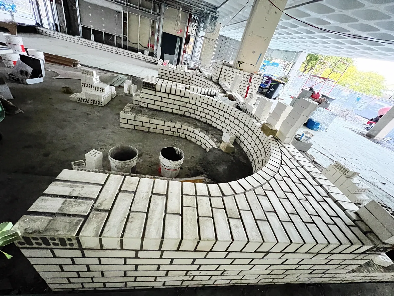 Amphitheatre seating wall part-built, showing the herringbone capping being laid over the curve.