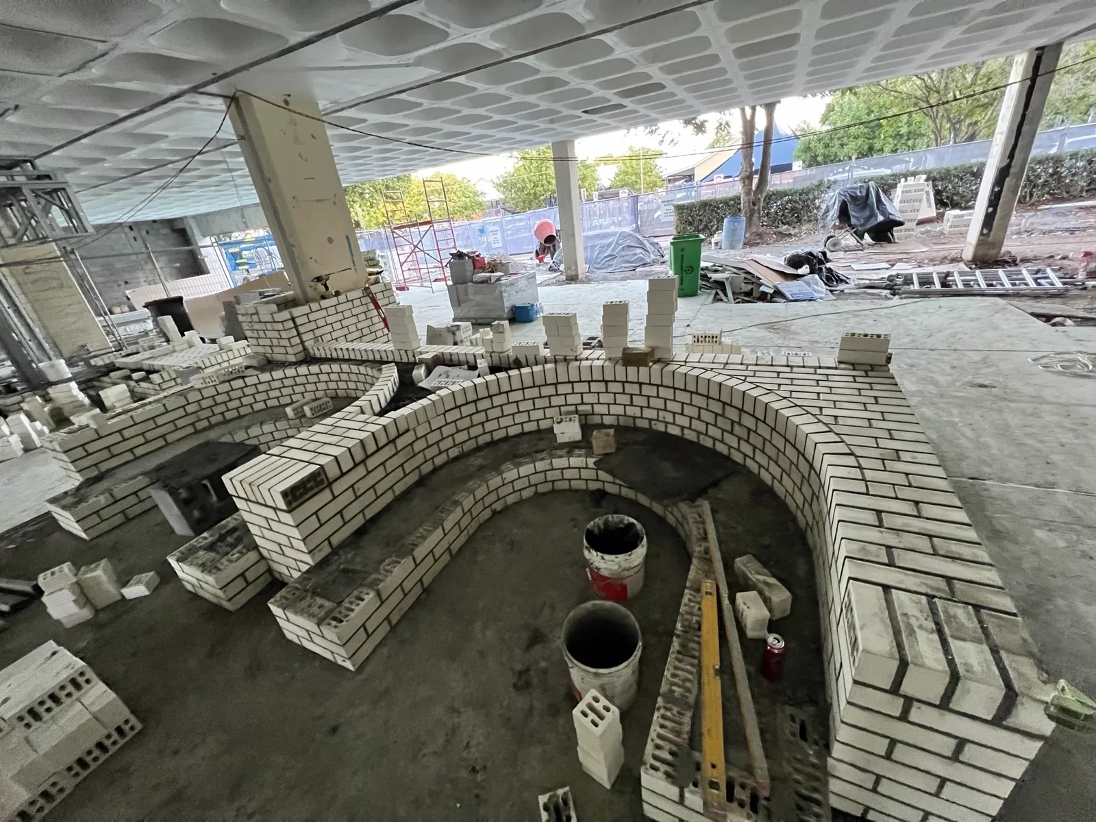Curved white brick amphitheatre walls under construction with materials staged around the setout.