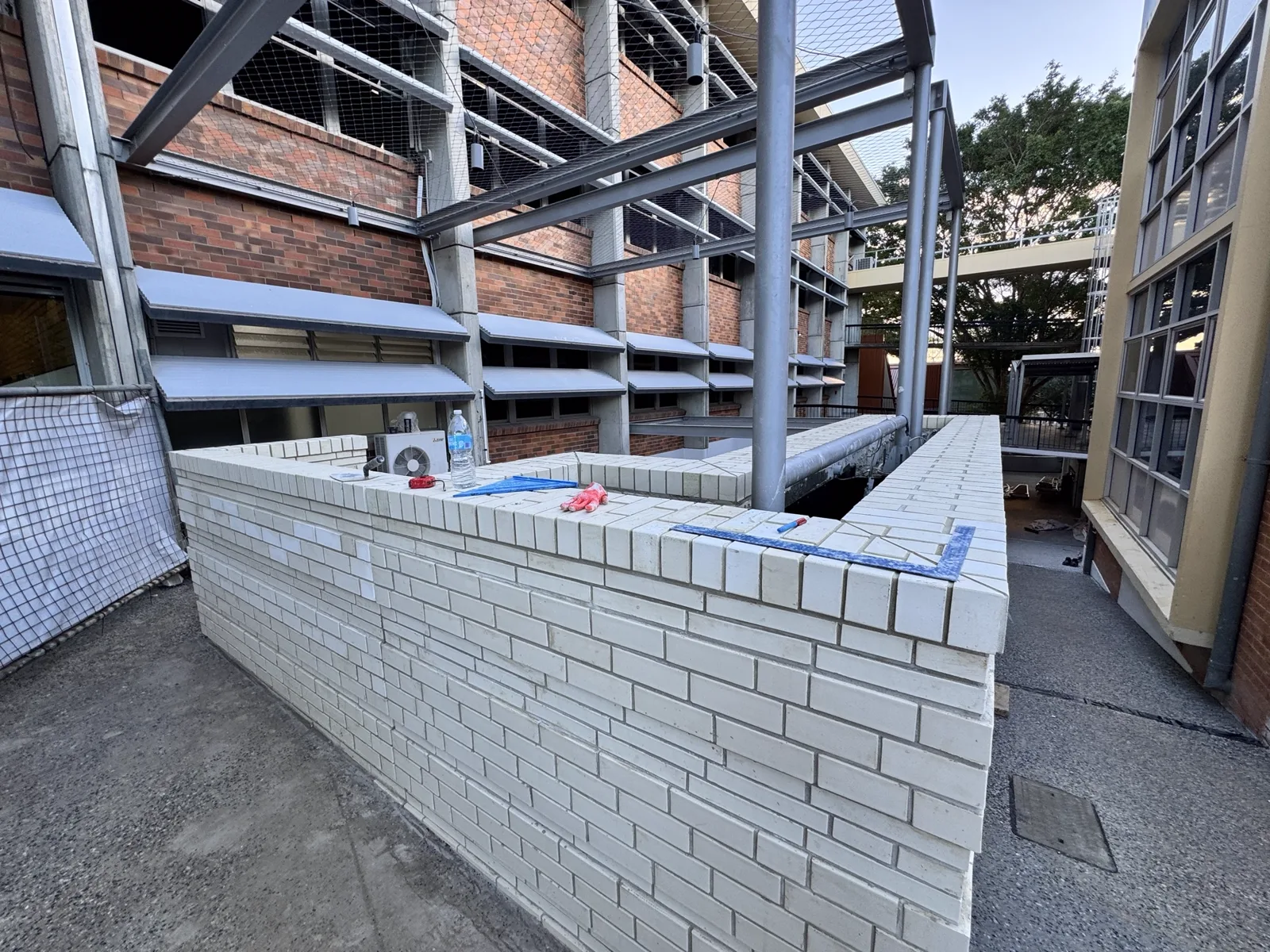 Glazed white brick courtyard walls with stack-bond capping, built around live school buildings and access ways.